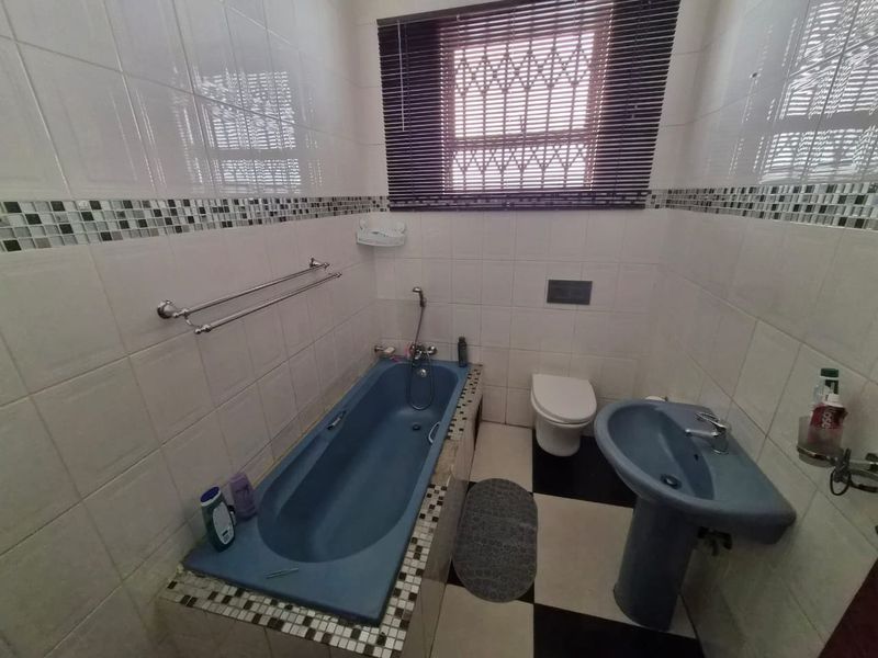 A functional bathroom featuring a built-in bathtub, pedestal basin, wall-mounted toilet, and tiled finishes throughout.