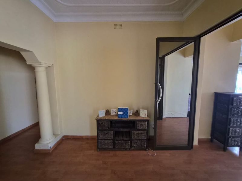 A living area featuring decorative ceiling cornices, a classic column archway, and laminate flooring, connecting to an adjacent room through a glass panel door.