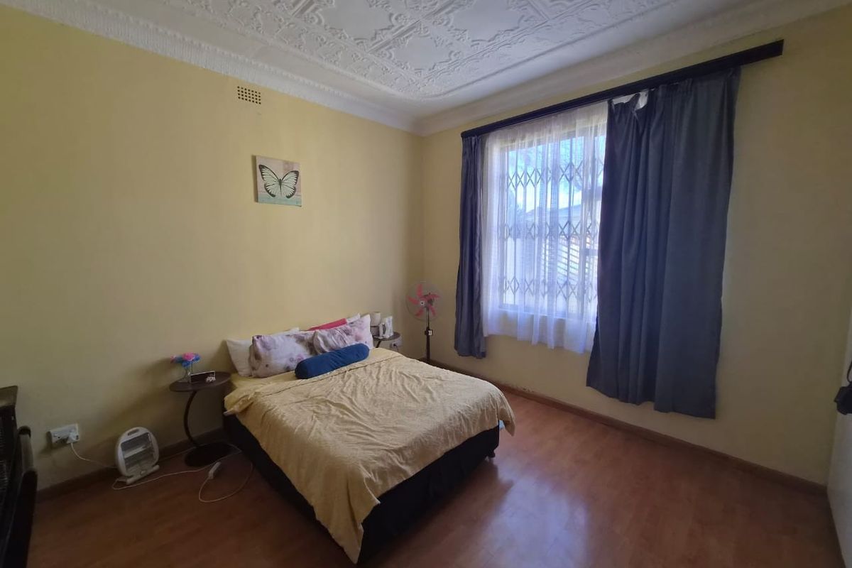A bedroom featuring an ornate plaster ceiling, laminate flooring, and a window fitted with a security gate.