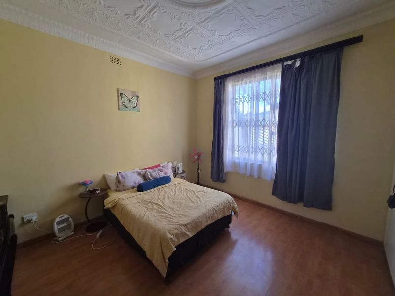 A bedroom featuring an ornate plaster ceiling, laminate flooring, and a window fitted with a security gate.
