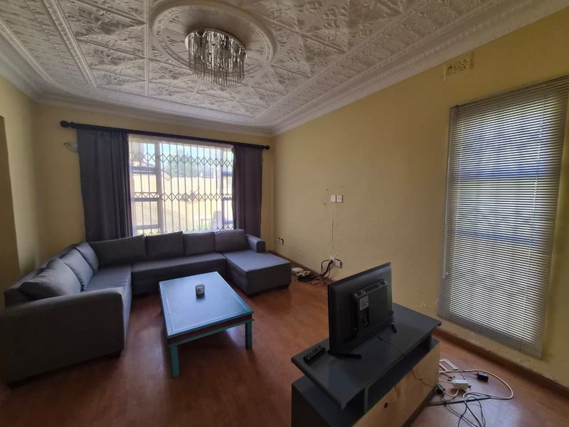 Living room featuring an ornate plaster ceiling, laminate flooring, and security bars on windows. The walls show visible signs of cracking and wear.
