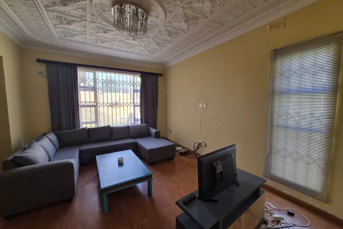 Living room featuring an ornate plaster ceiling, laminate flooring, and security bars on windows. The walls show visible signs of cracking and wear.
