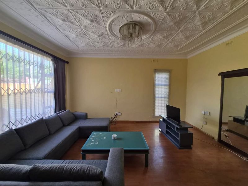 Spacious living room featuring a distinctive ornate pressed metal ceiling, crystal chandelier, and large windows with security gates.