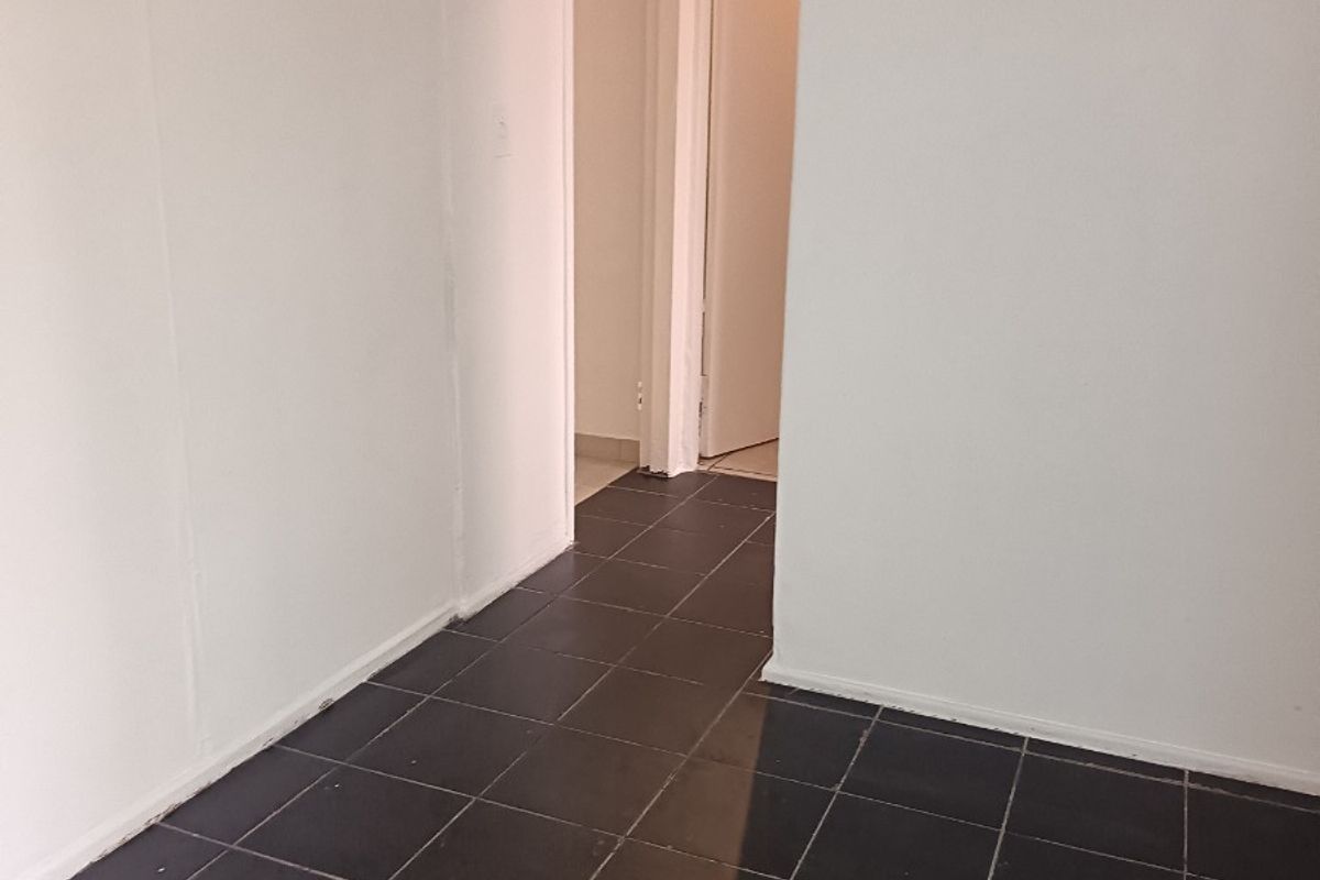 A vacant hallway featuring dark tiled flooring and an arched transition leading to adjacent rooms.