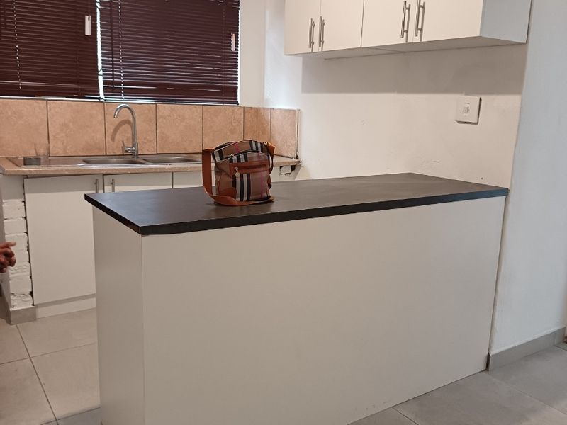 A functional kitchen featuring white cabinetry, a dark laminate breakfast bar, tiled backsplash, and neutral floor tiles, offering a clean and simple layout.