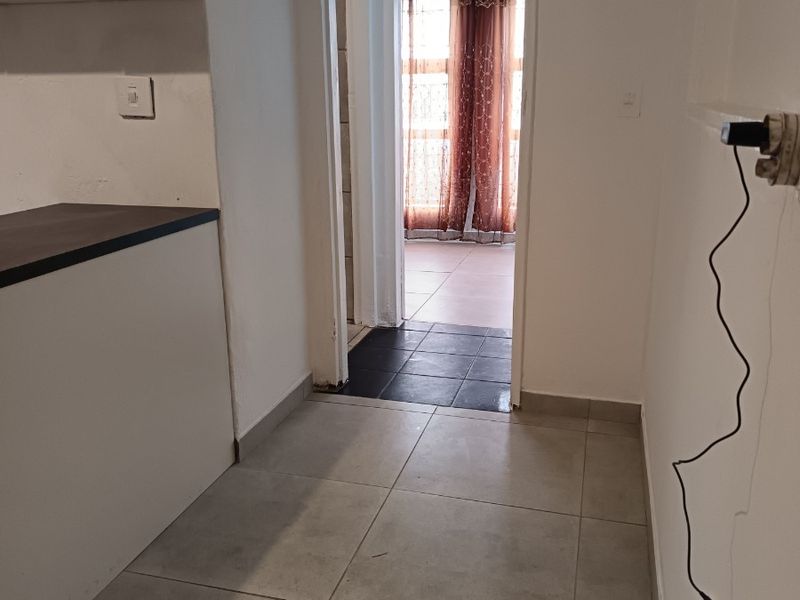 A functional kitchen area featuring neutral tiled flooring and built-in cabinetry, leading through to an adjacent room with dark floor tiles.