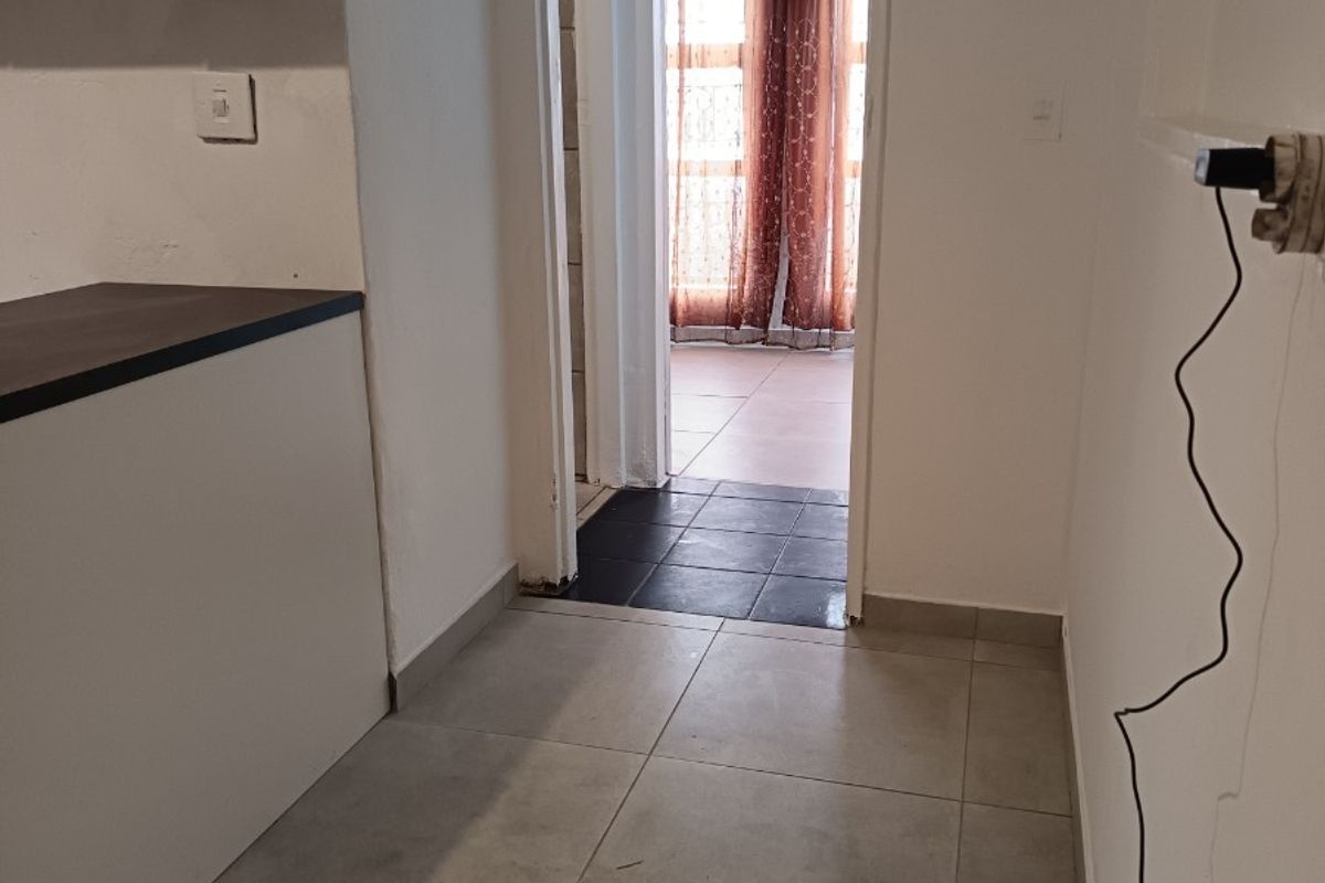 A functional kitchen area featuring neutral tiled flooring and built-in cabinetry, leading through to an adjacent room with dark floor tiles.