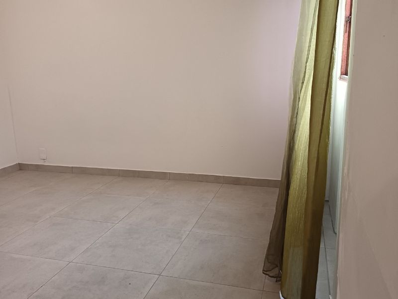 A vacant bedroom featuring neutral tiled flooring and a window with existing curtaining, providing a clean and blank canvas for personalization.