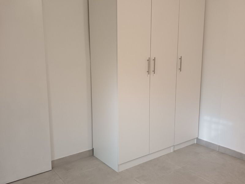 A clean, minimalist bedroom featuring neutral tiled flooring and a modern white built-in wardrobe.