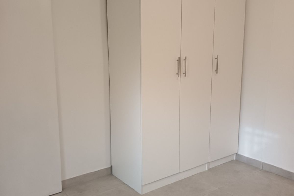 A clean, minimalist bedroom featuring neutral tiled flooring and a modern white built-in wardrobe.