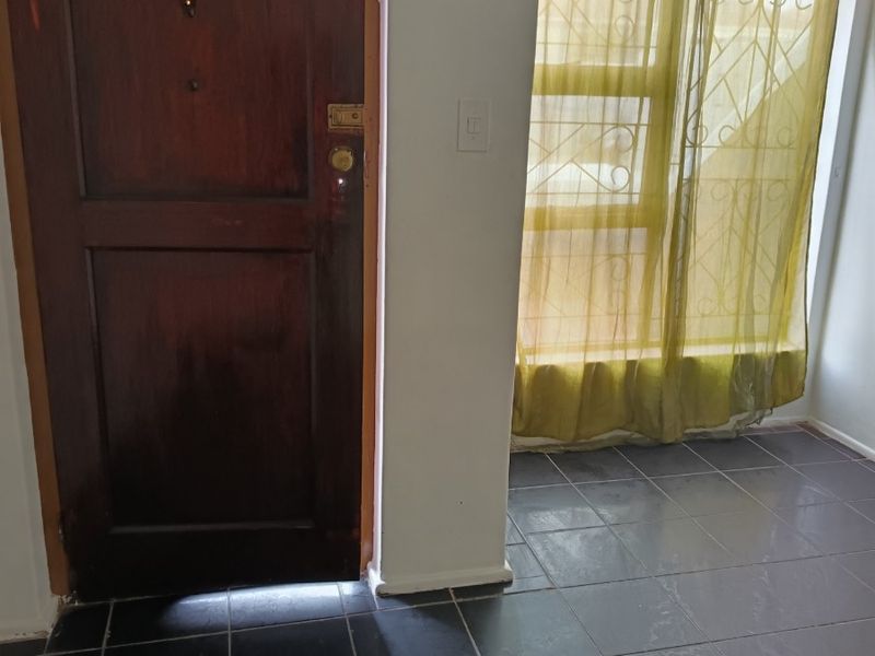 An entry area featuring dark tiled flooring, a solid timber door, and a window fitted with security bars.