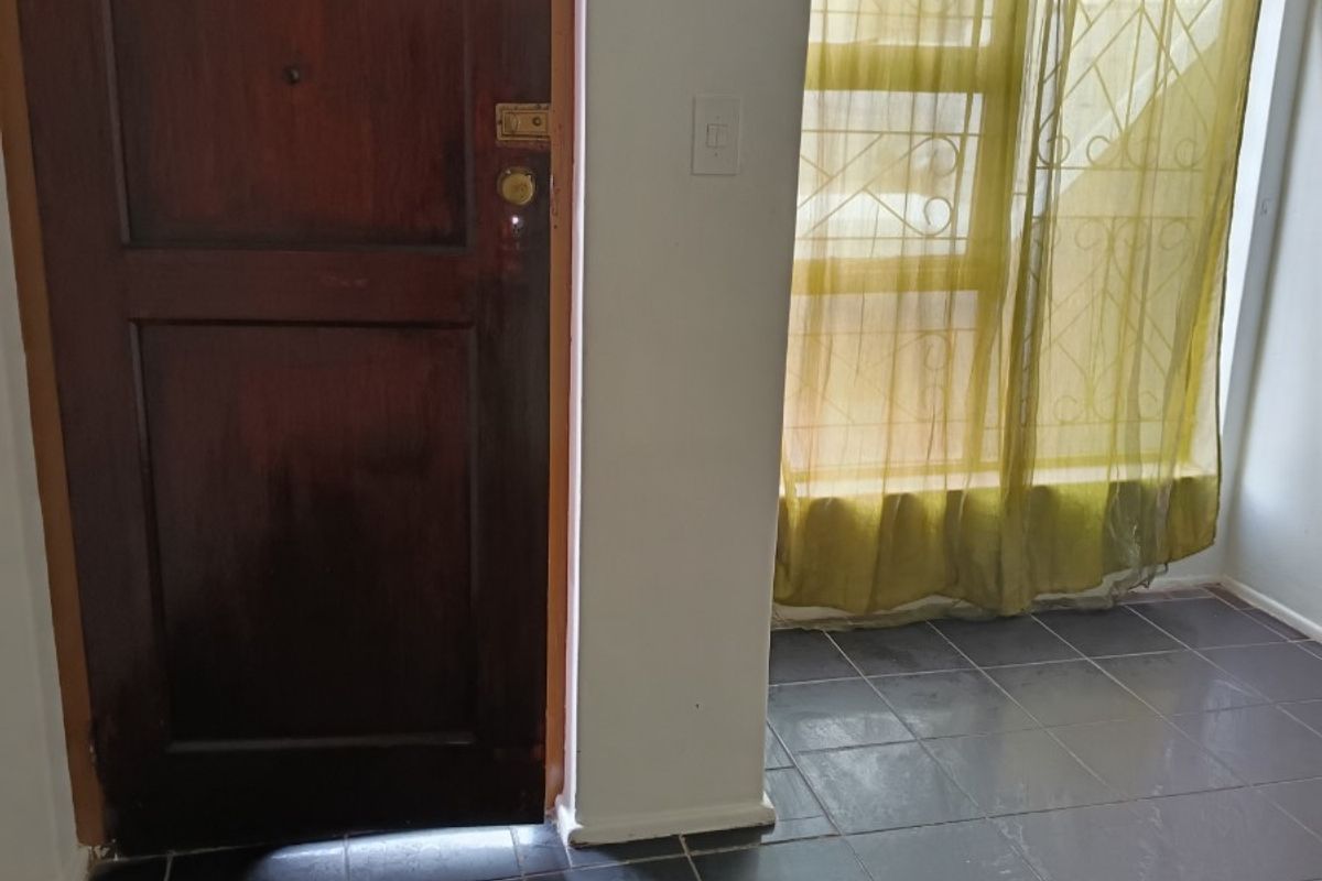An entry area featuring dark tiled flooring, a solid timber door, and a window fitted with security bars.