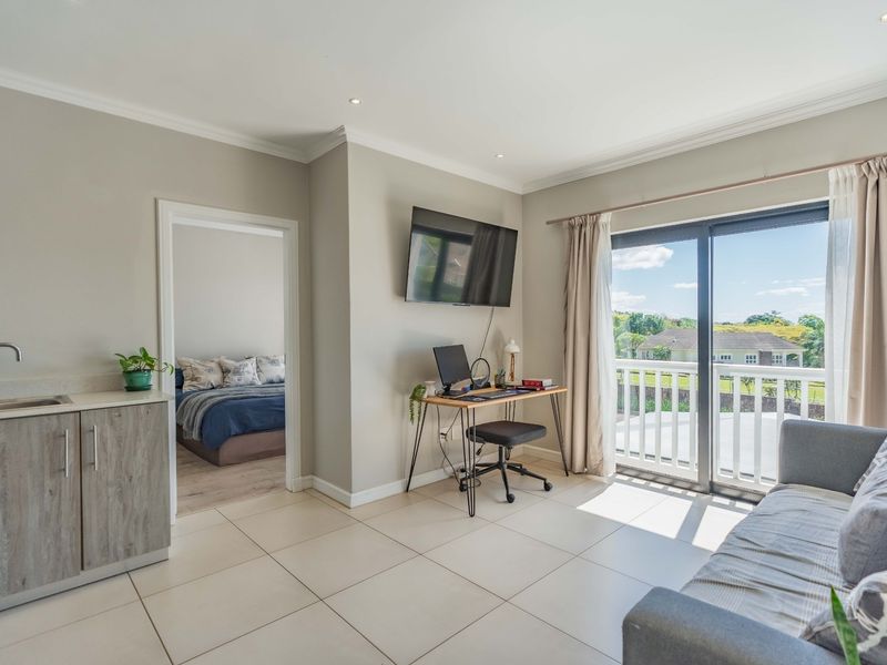 Open plan living area featuring a compact kitchenette, tiled flooring, and sliding glass doors leading to a balcony with scenic views.