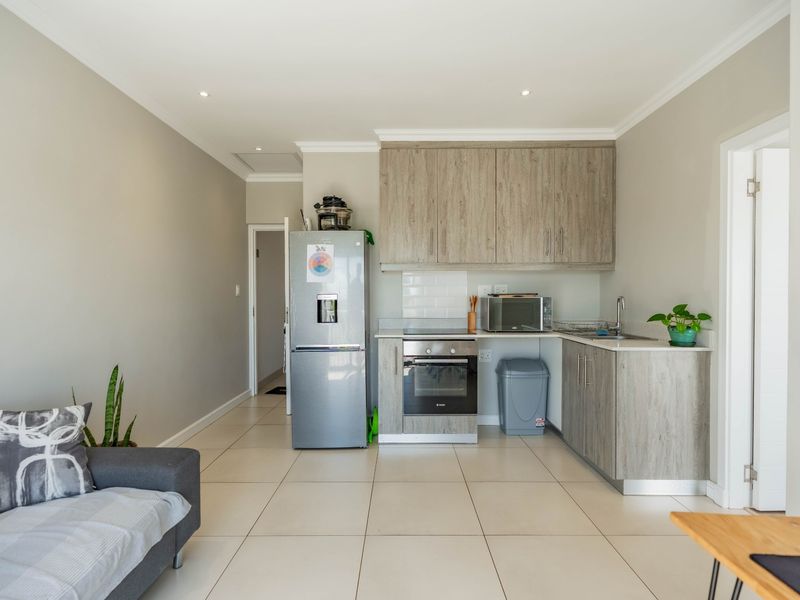 An open-plan living area featuring a modern kitchen with wood-look cabinetry, built-in oven, hob, and tiled flooring throughout.