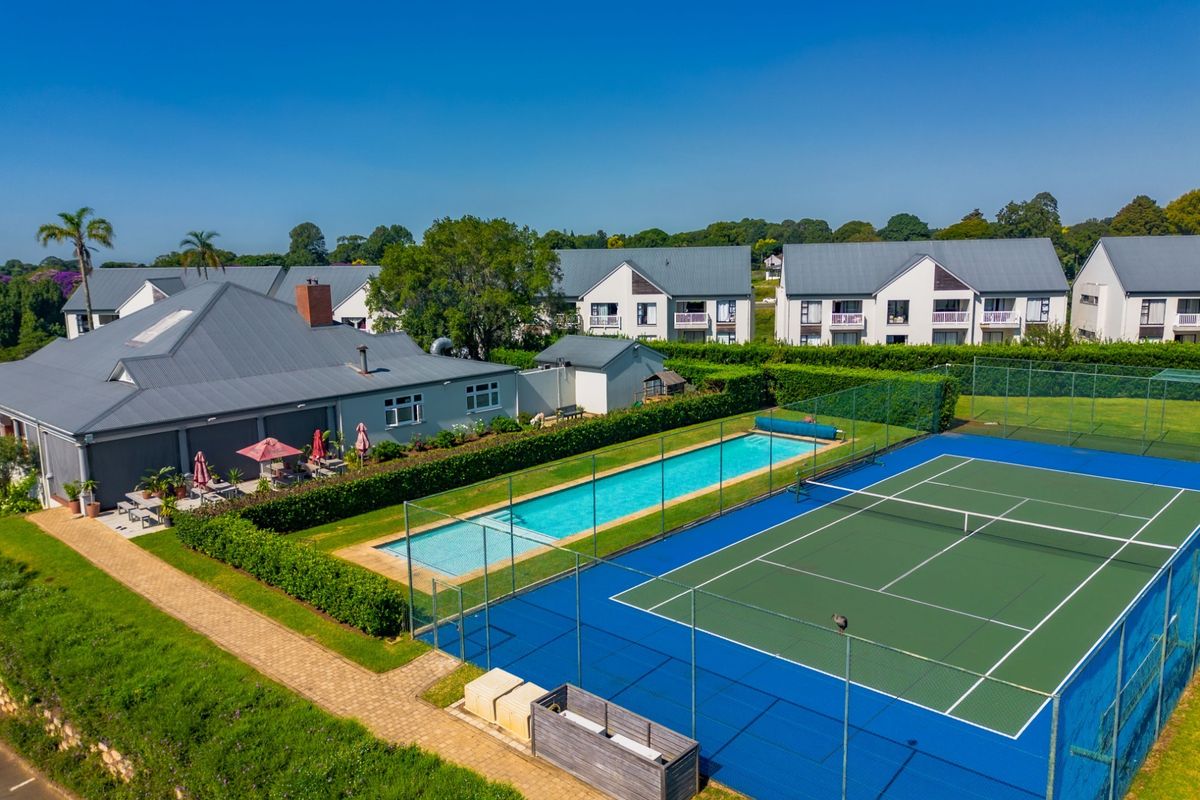 Aerial view of the apartment complex featuring a well-maintained swimming pool, tennis court, and landscaped garden areas.