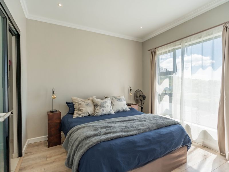 A well-maintained bedroom featuring neutral wall tones, recessed downlighting, coving, and light-toned laminate flooring with natural light from a large window.