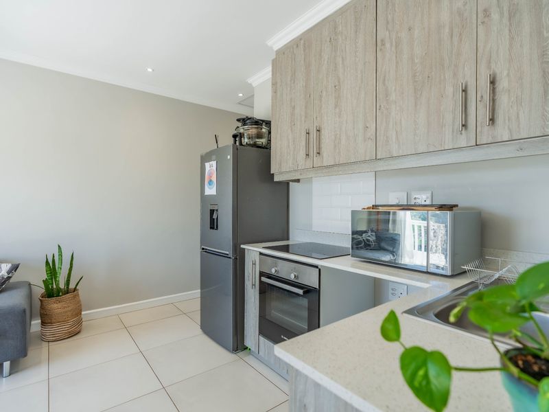 Modern open-plan kitchen featuring light wood-grain cabinetry, stone countertops, subway tile backsplash, and integrated appliances, seamlessly flowing into the living area.
