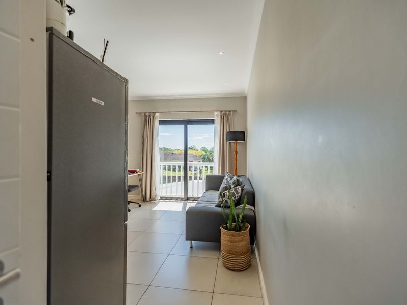 A bright living area featuring large format floor tiles and a sliding glass door providing direct access to an outdoor balcony.