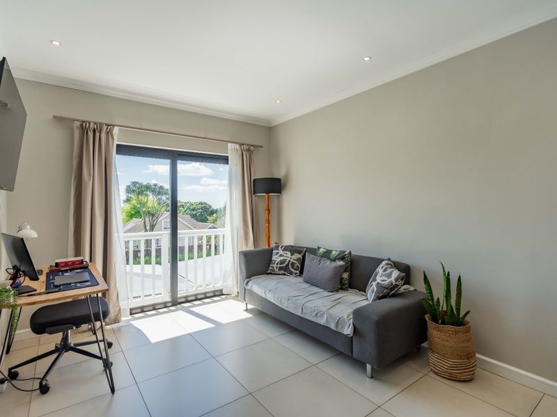A bright living room featuring large sliding glass doors leading to a balcony, neutral tiled flooring, and recessed downlighting.