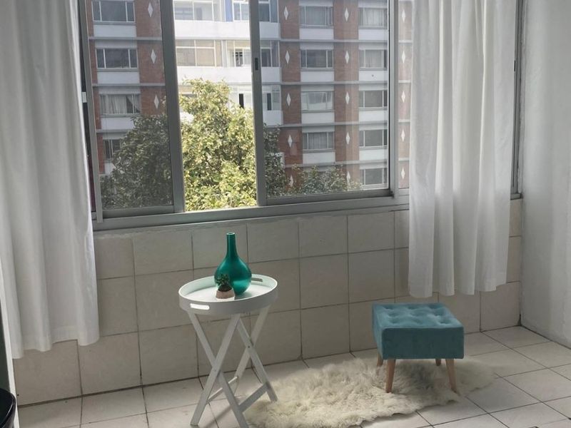 Enclosed balcony area featuring tiled flooring and wall cladding with large sliding windows overlooking the surrounding apartment complex.