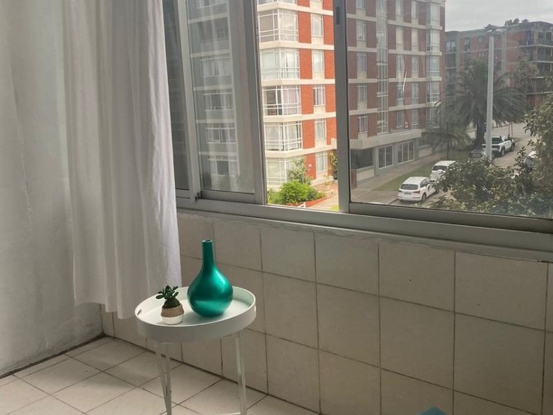 A compact balcony area featuring tiled flooring and wall cladding with large sliding windows offering an urban neighbourhood view.