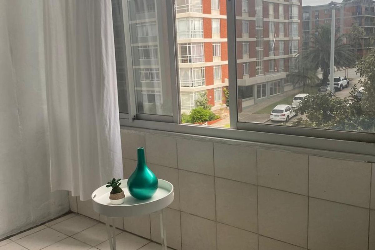 A compact balcony area featuring tiled flooring and wall cladding with large sliding windows offering an urban neighbourhood view.