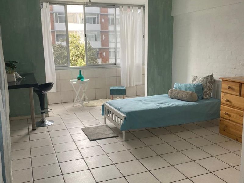 A bedroom featuring tiled flooring, a large window providing natural light, and a ceiling-mounted spotlight fixture.
