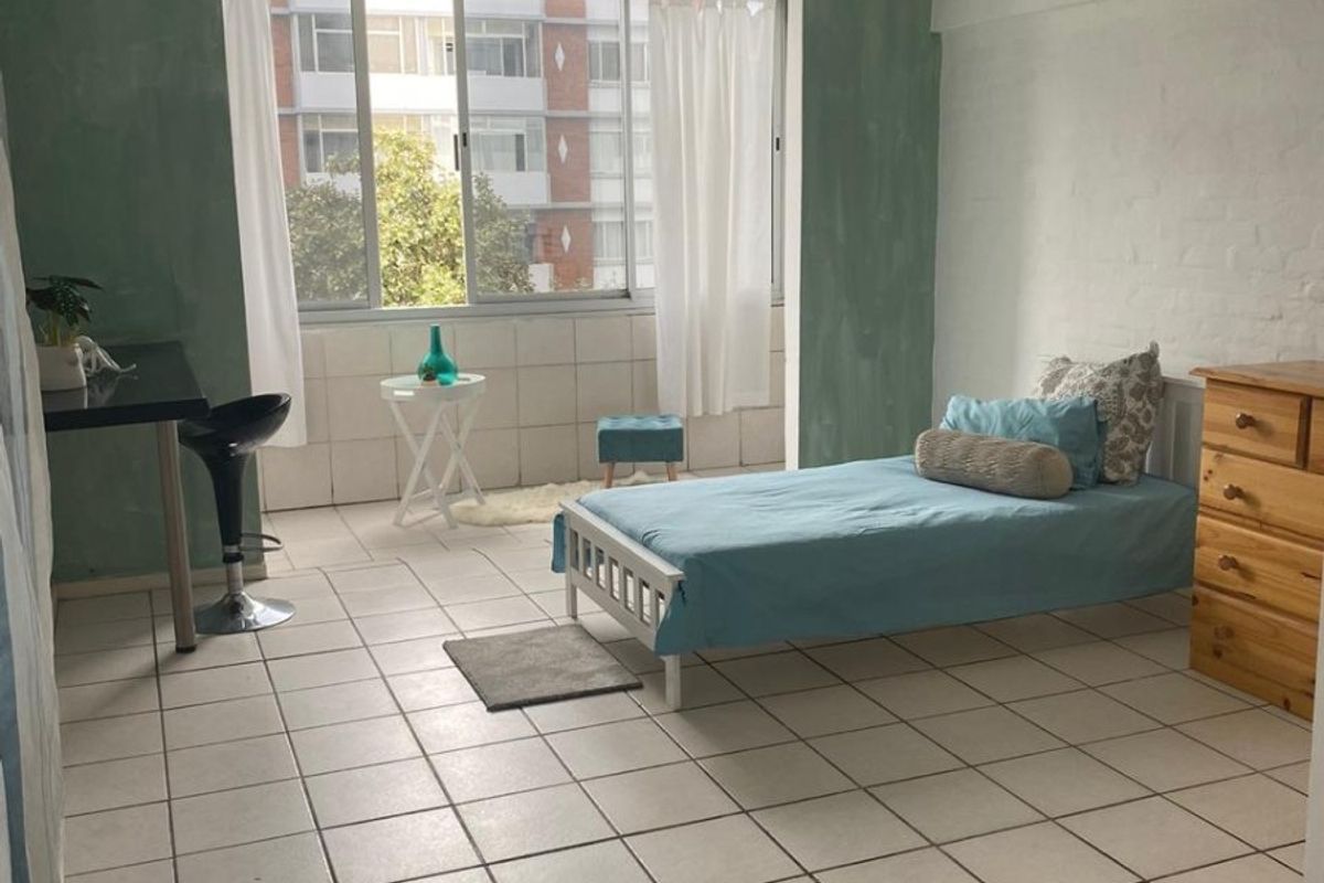 A bedroom featuring tiled flooring, a large window providing natural light, and a ceiling-mounted spotlight fixture.