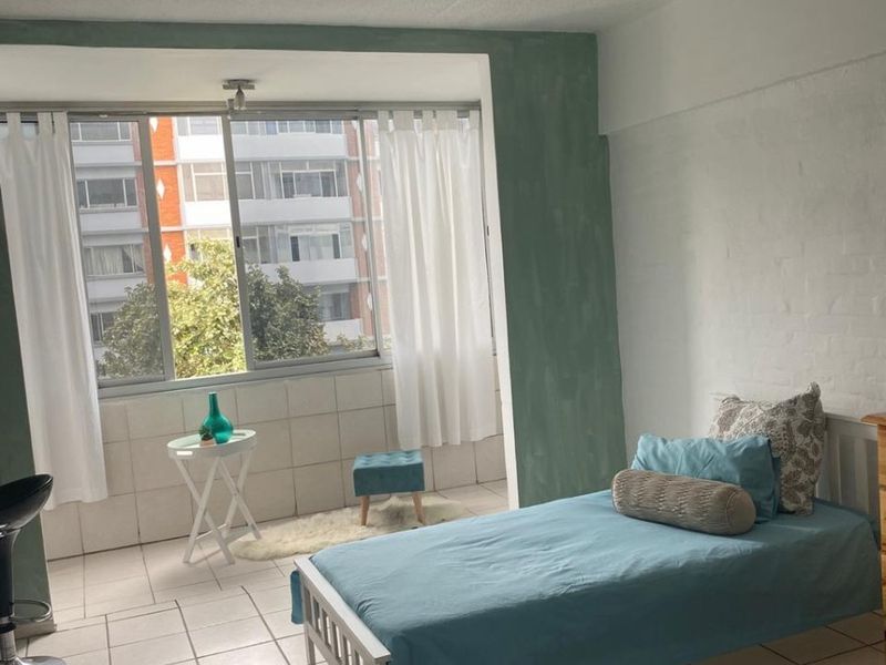 A bedroom featuring tiled flooring and a large window with natural light. The space has a simple layout with painted brick wall accents.