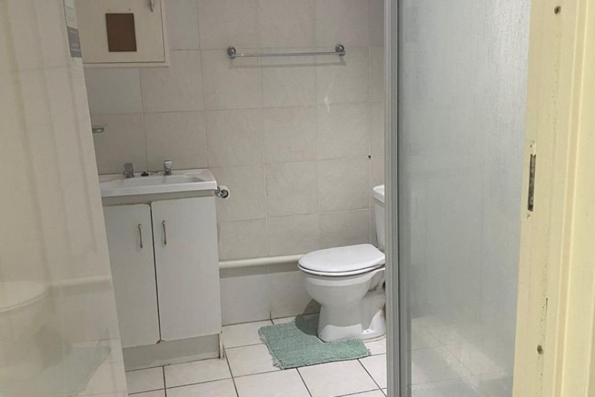 A functional bathroom featuring a vanity cabinet, toilet, and a glass-enclosed shower with tiled finishes throughout.