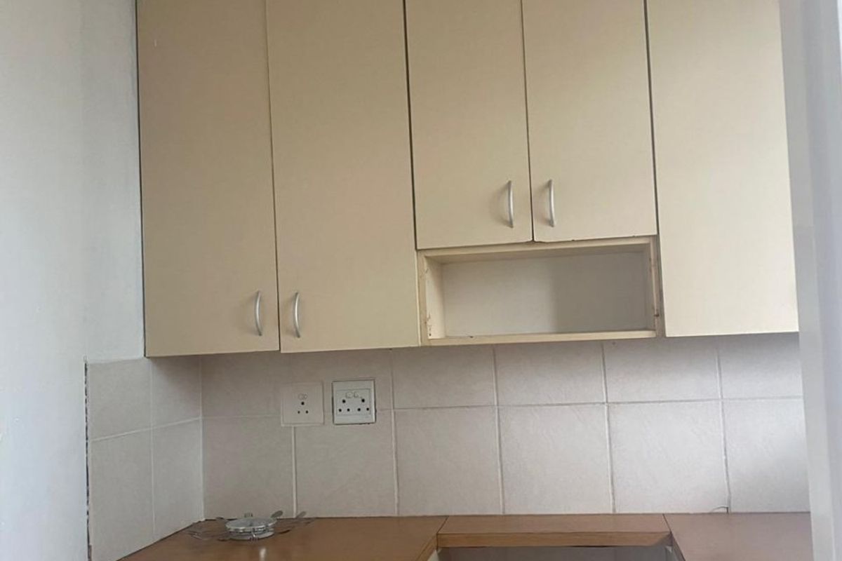 A compact kitchen area featuring built-in cabinetry, laminate countertops, and tiled backsplash, currently vacant and ready for updates.