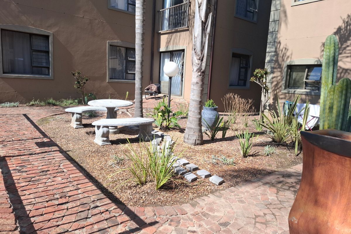 A communal rear courtyard area featuring brick paving, established trees, and landscaped garden beds between apartment building wings.