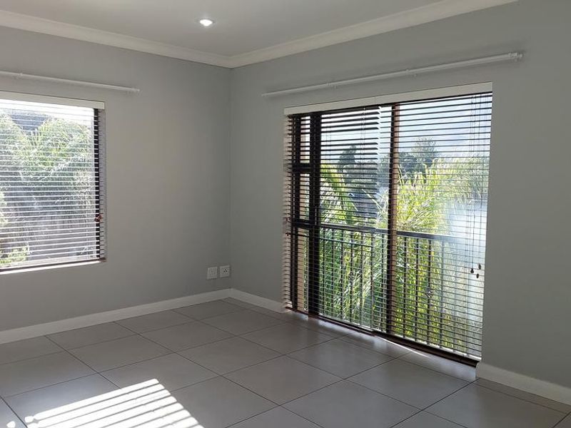 A bright, empty bedroom featuring neutral grey walls, large tiled flooring, and a sliding glass door leading to an outdoor area.