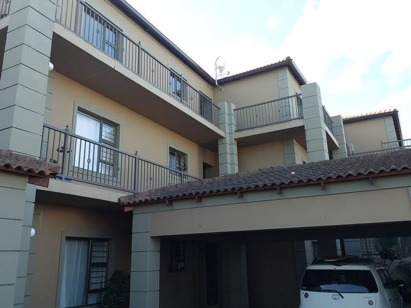 Exterior view of a multi-story apartment complex featuring balconies with metal railings, a tiled roof, and a covered carport area.