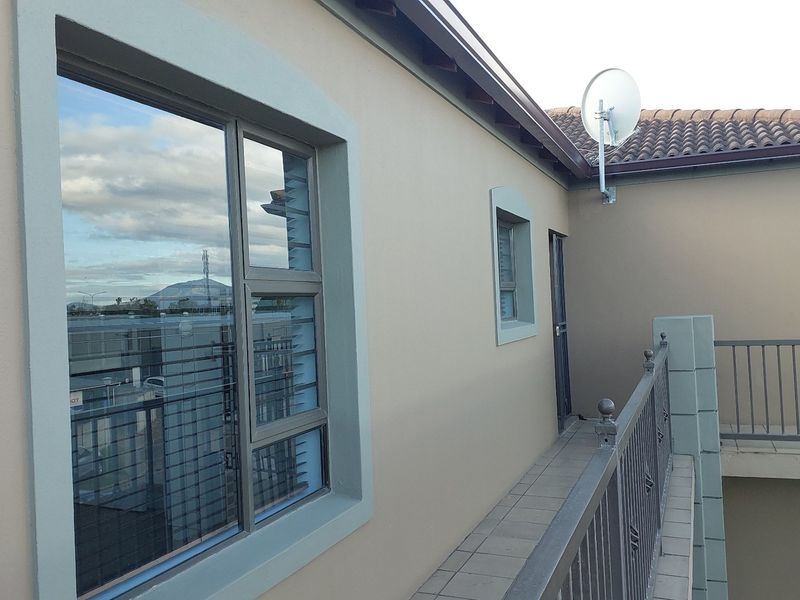 An exterior view of an apartment balcony featuring tiled flooring, metal balustrades, and aluminium window frames.