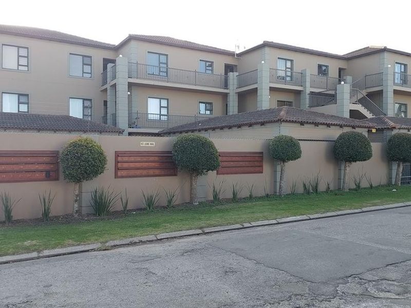 Front exterior view of a multi-story apartment complex featuring a perimeter wall, secure gated access, and private balconies for each unit.
