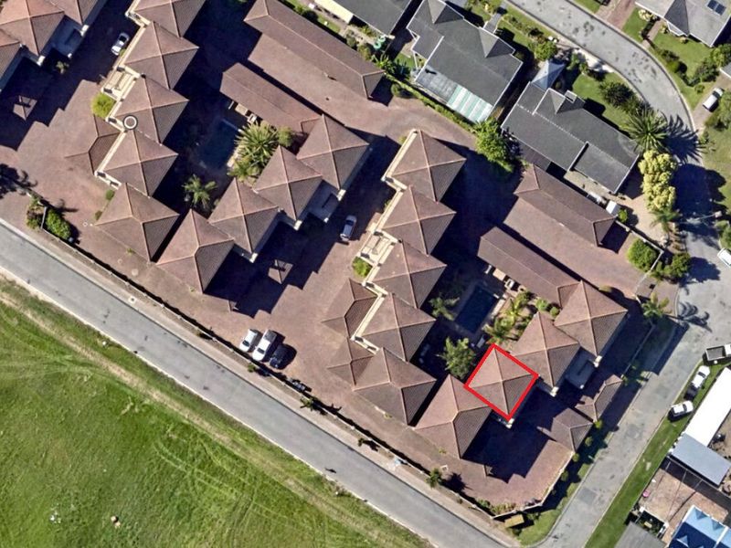 Aerial view of the apartment complex showing the layout, tiled roof structures, communal pool area, and surrounding paved access roads.