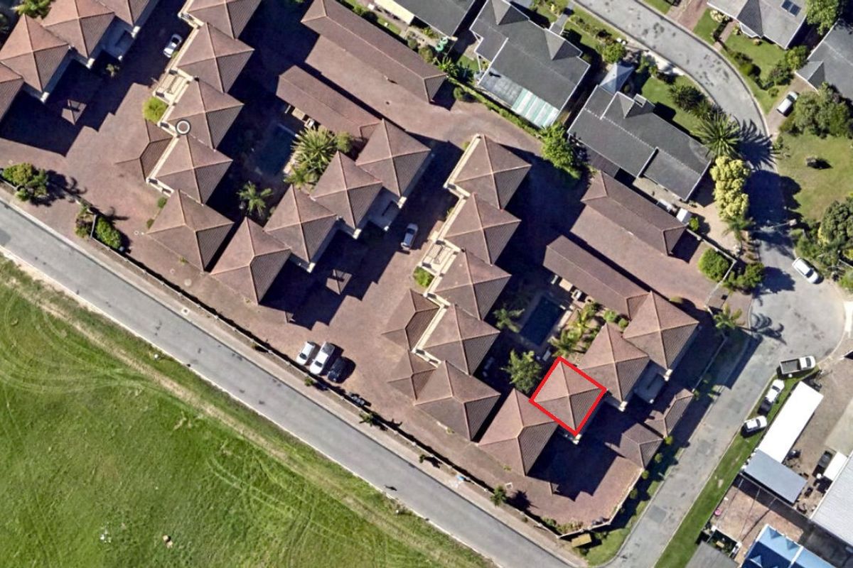 Aerial view of the apartment complex showing the layout, tiled roof structures, communal pool area, and surrounding paved access roads.