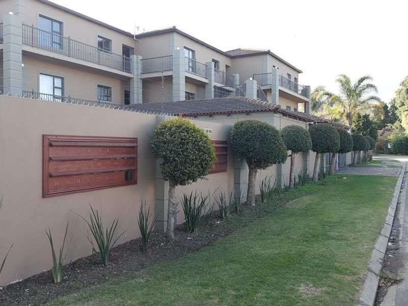 Street view of the apartment complex featuring a secure perimeter wall with integrated post boxes, electric fencing, and well-maintained landscaped verge.