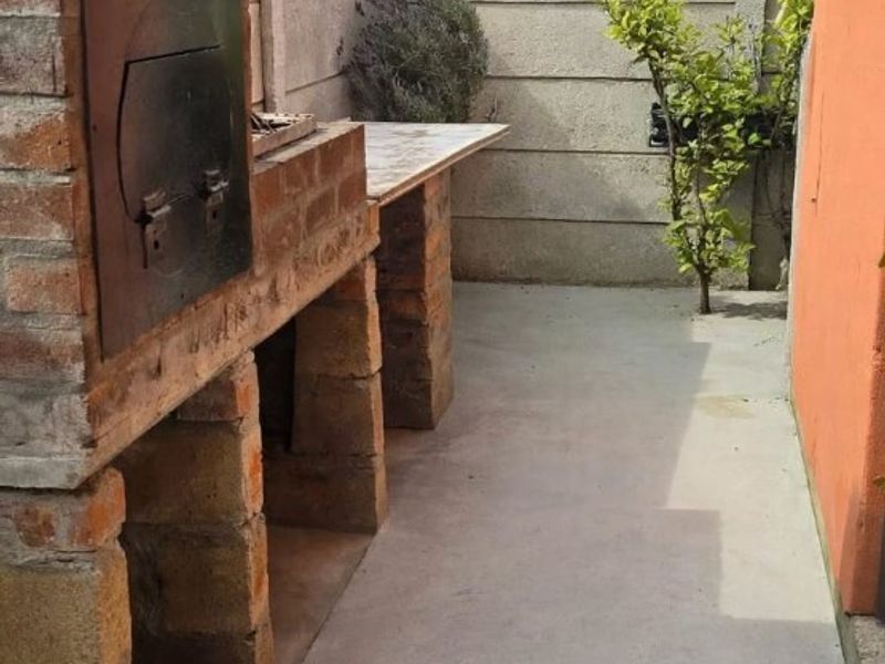 Outdoor patio area featuring a built-in brick braai and concrete flooring, enclosed by a precast boundary wall.