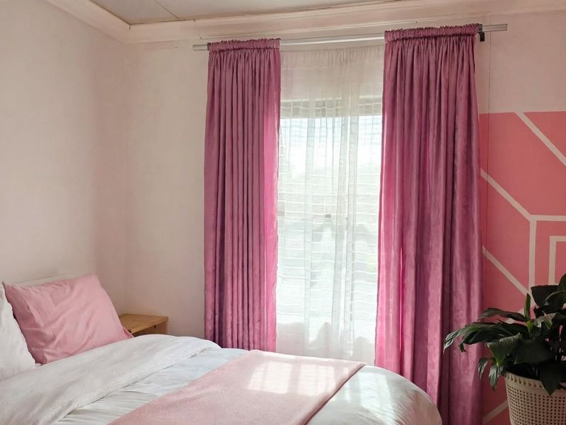 A bedroom featuring a window with curtains and a decorative painted wall accent.