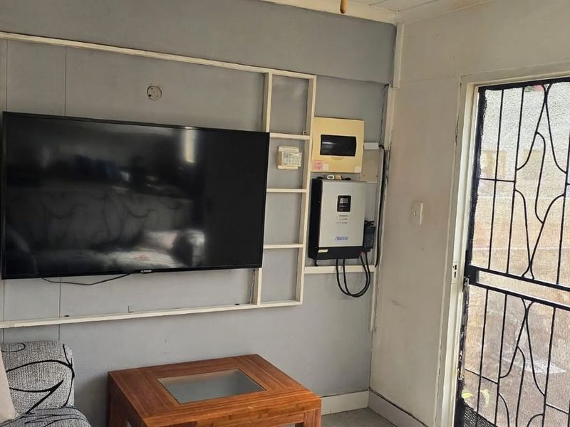 Living area featuring a security gate, wall-mounted inverter system, and decorative shelving unit.