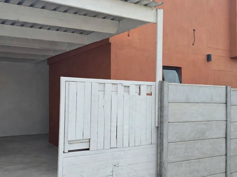 A covered carport area featuring a concrete boundary wall and a timber gate entrance.