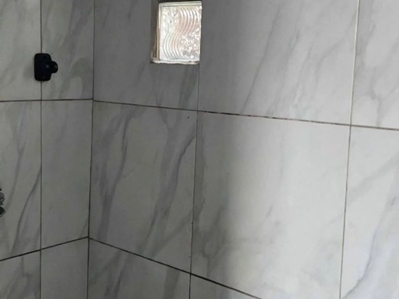 A tiled shower enclosure featuring a modern rain shower head, a built-in bench, and a small glass block window for natural light.
