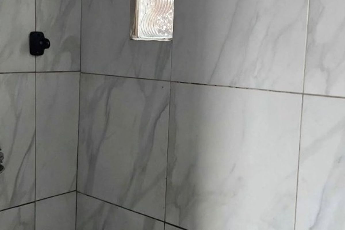A tiled shower enclosure featuring a modern rain shower head, a built-in bench, and a small glass block window for natural light.