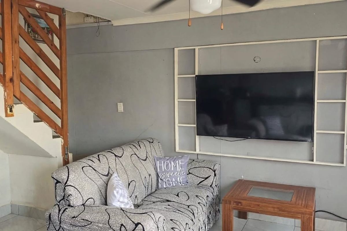 Living room featuring a wooden staircase, built-in wall shelving, and an installed inverter system. The space shows signs of wear and requires cosmetic updates.