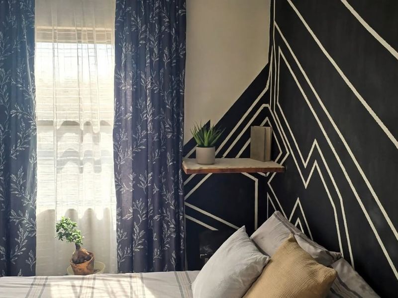 A bedroom featuring a window with curtains and a decorative painted accent wall.