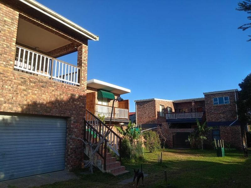 Rear view of a multi-story face brick residential building featuring balconies, external staircases, and integrated garage access with a shared garden area.
