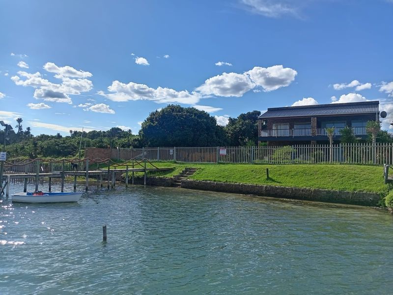 Rear view of a two-story brick house featuring a private timber jetty, stone retaining wall, and direct water access.