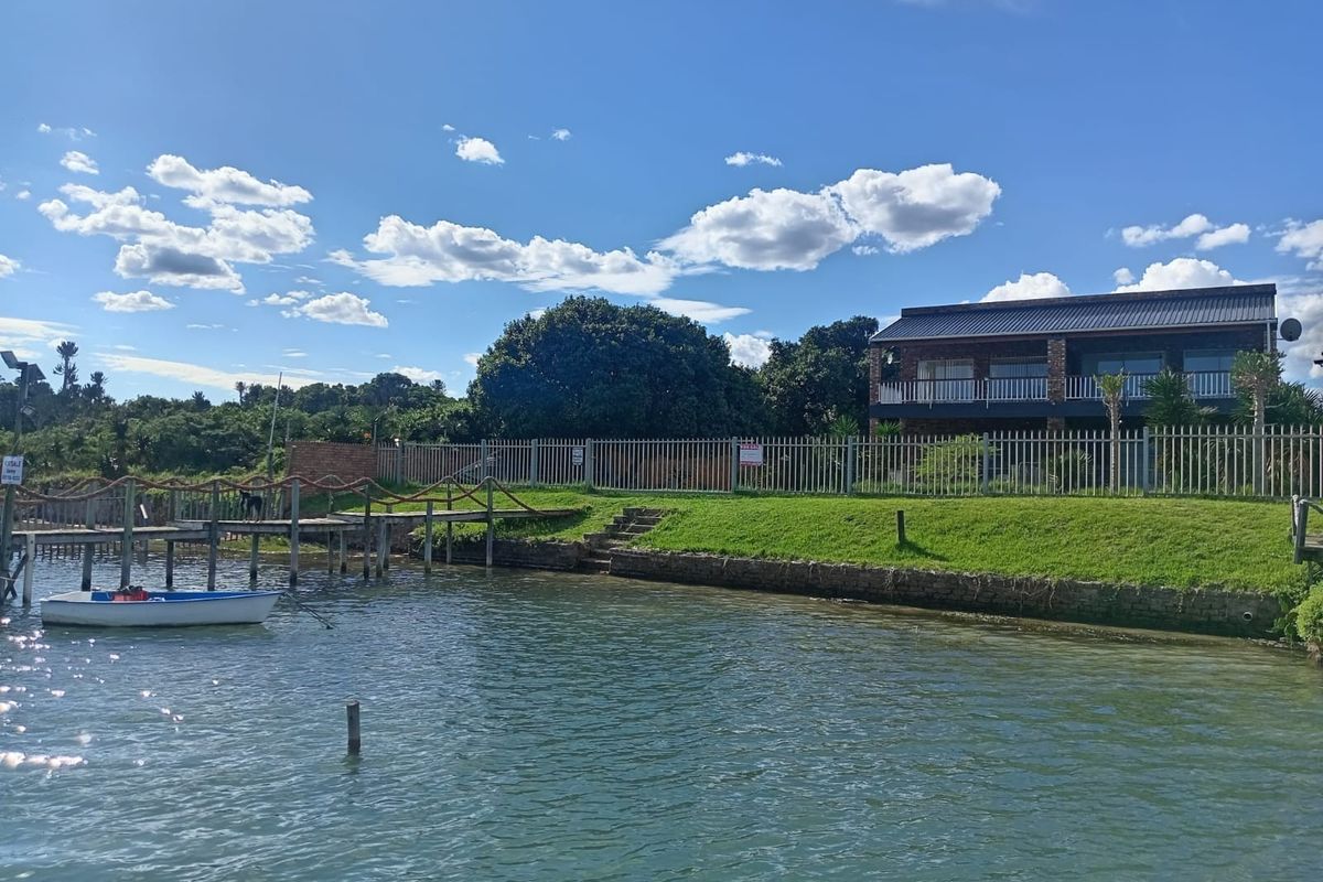 Rear view of a two-story brick house featuring a private timber jetty, stone retaining wall, and direct water access.